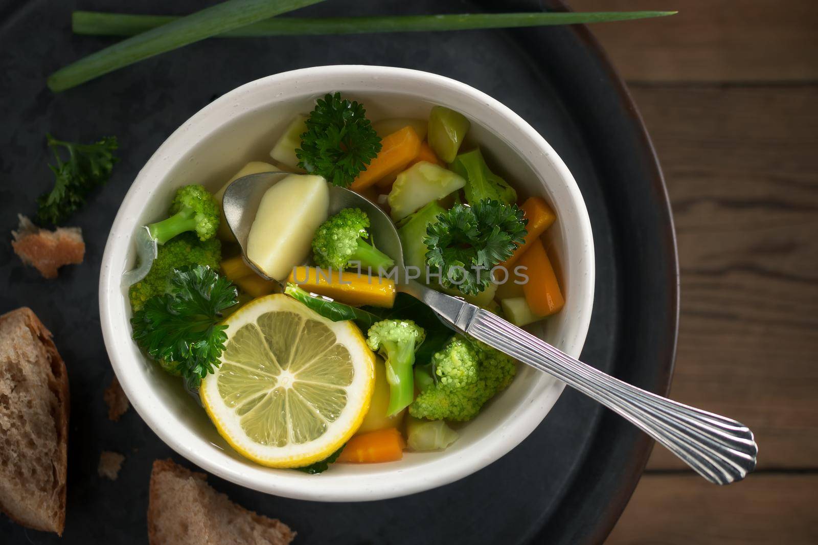 Vegetarian vegetable soup with carrots, broccoli and parsley in a light bowl on a metal tray on a wooden table by galsand