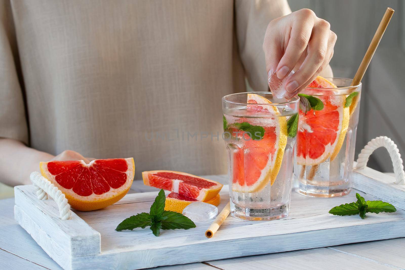 Girl cooking summer refreshing fruit cocktail with grapefruit slices and mint by galsand