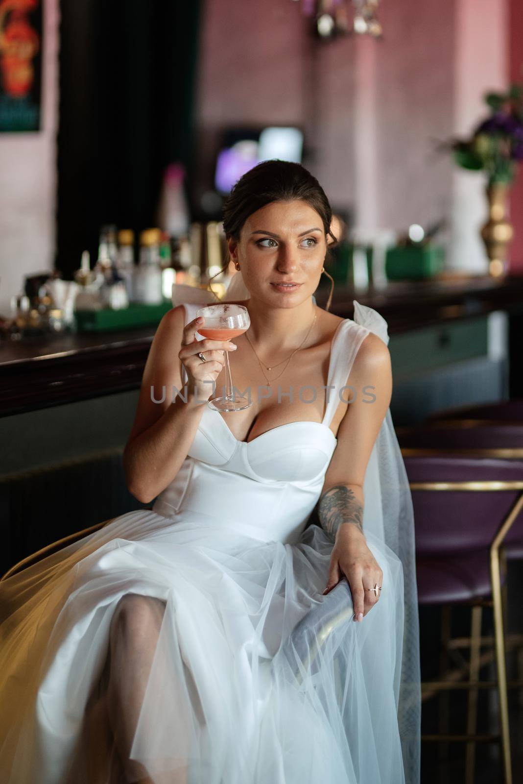 bride inside the cocktail bar at the bar in a bright atmosphere with a glass of drink