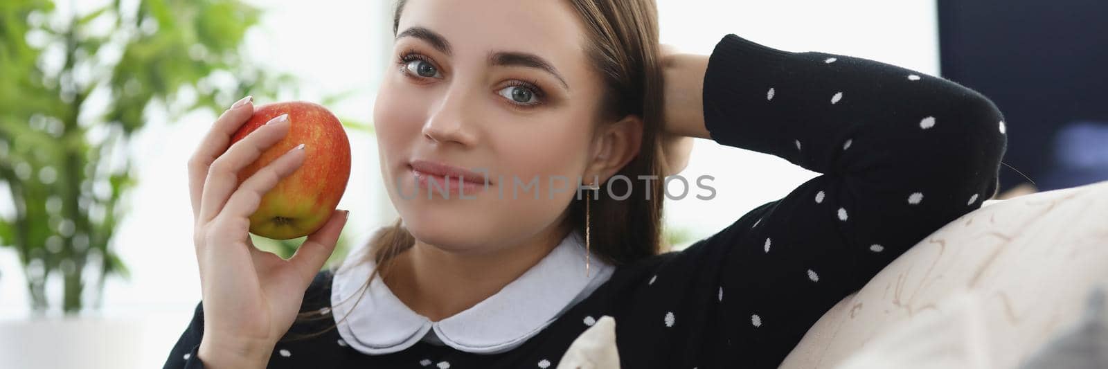 Portrait of pretty young woman sit comfy on couch at home, fresh apple fruit as snack. Lovely girl having lunch. Chill, relaxation, weekend fun concept