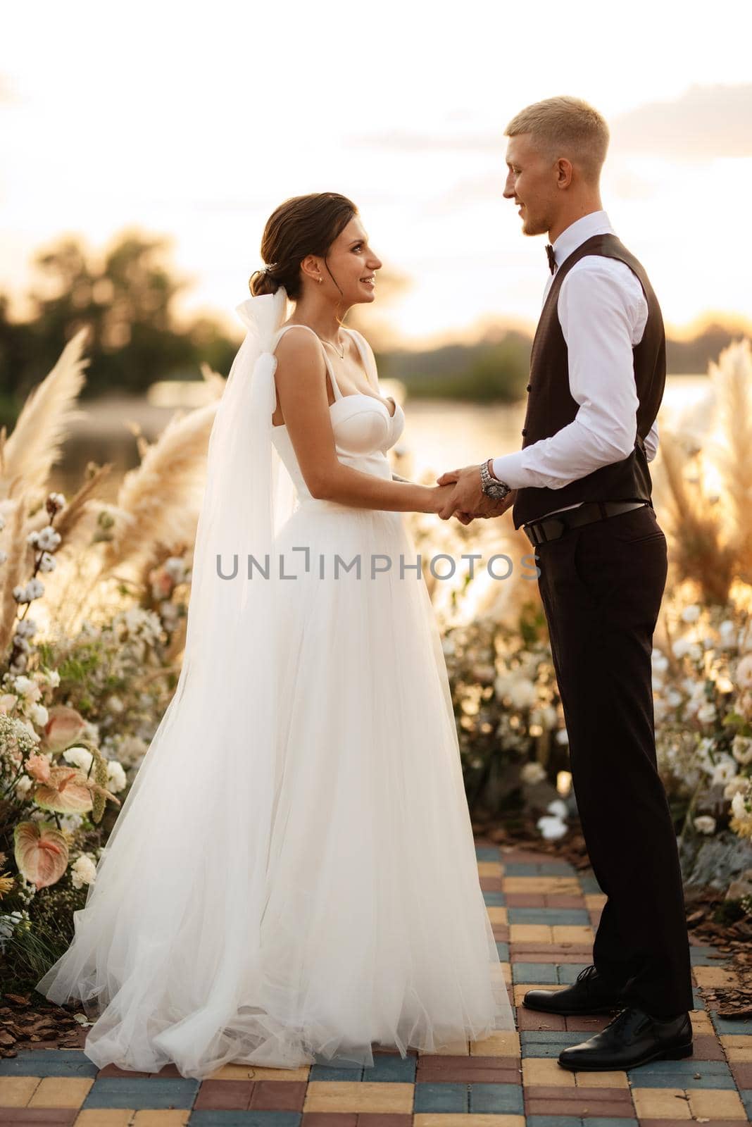 bride and groom against the backdrop of a yellow sunset on a pier near the river