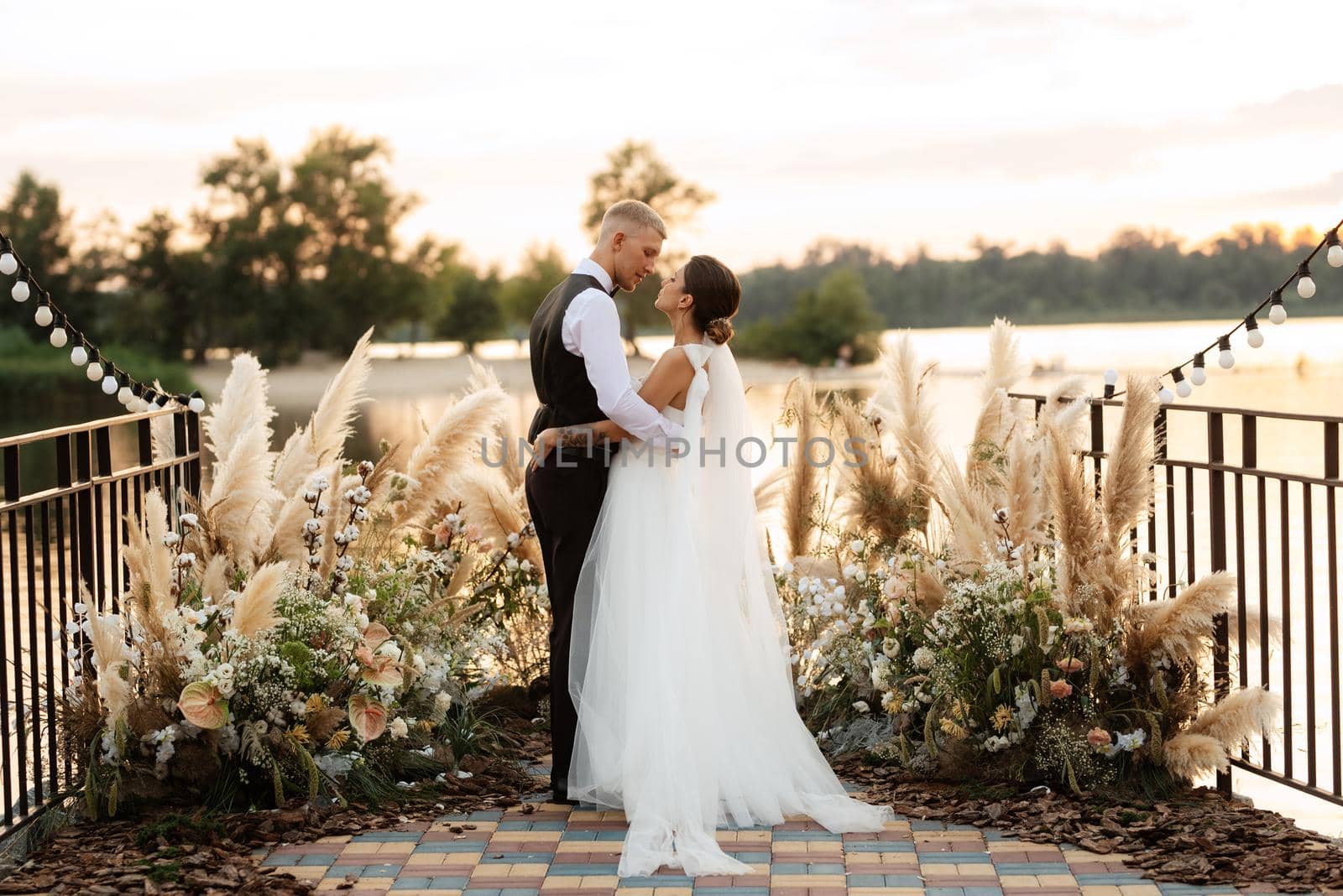 bride and groom against the backdrop of a yellow sunset on a pier near the river