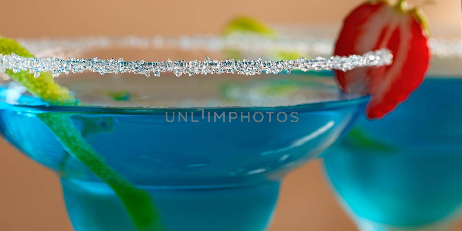Two glasses with blue margarita cocktail garnished with lime zest and strawberries, selective focus by galsand