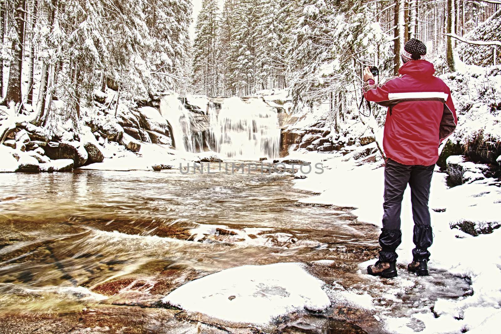 Nature photographer takes picture of winter snow landscape set in woodland with waterfall