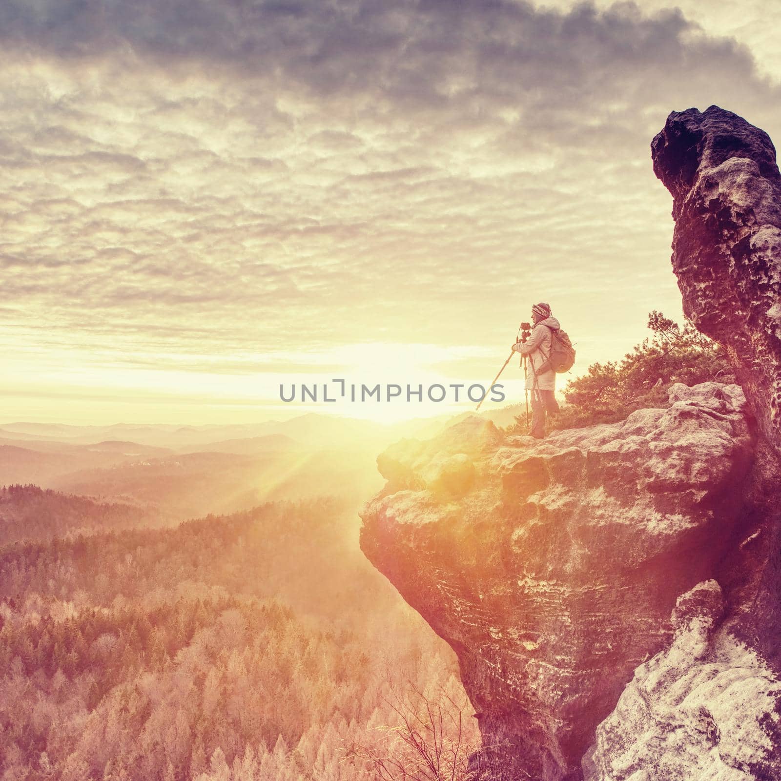 Photographer is taking pictures with camera in morning hills. Nature landscape photographer with photo equipment on rock. Silhouette of hiker woman