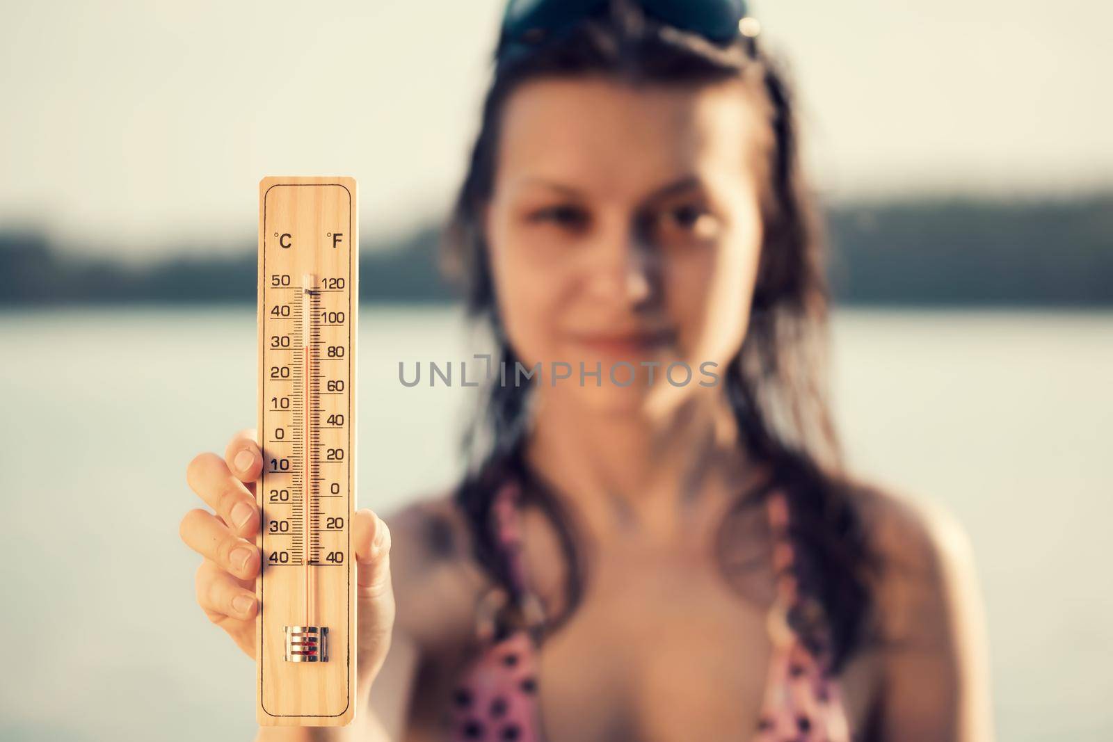 Beautiful young woman with a thermometer in her hand on the background of the lake. Summer vacation and heat concept, selective focus by galsand