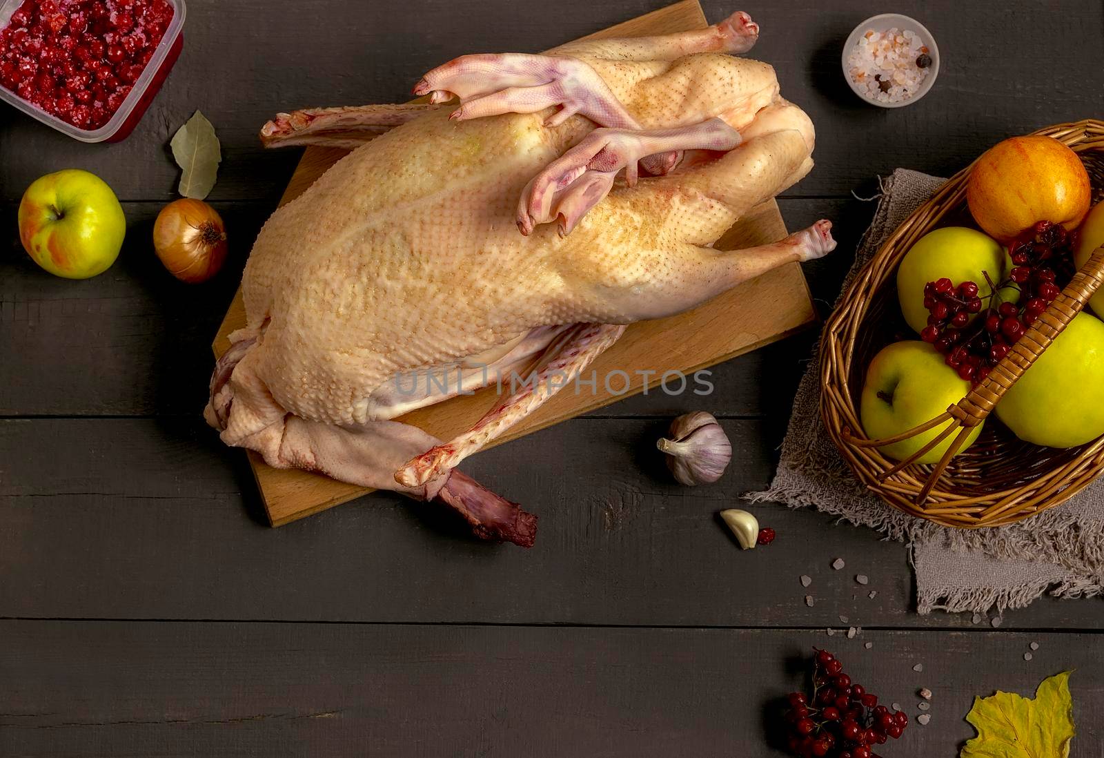 On the kitchen table there is a duck carcass next to the products for its further preparation: apples and berries for stuffing, spices and vegetables