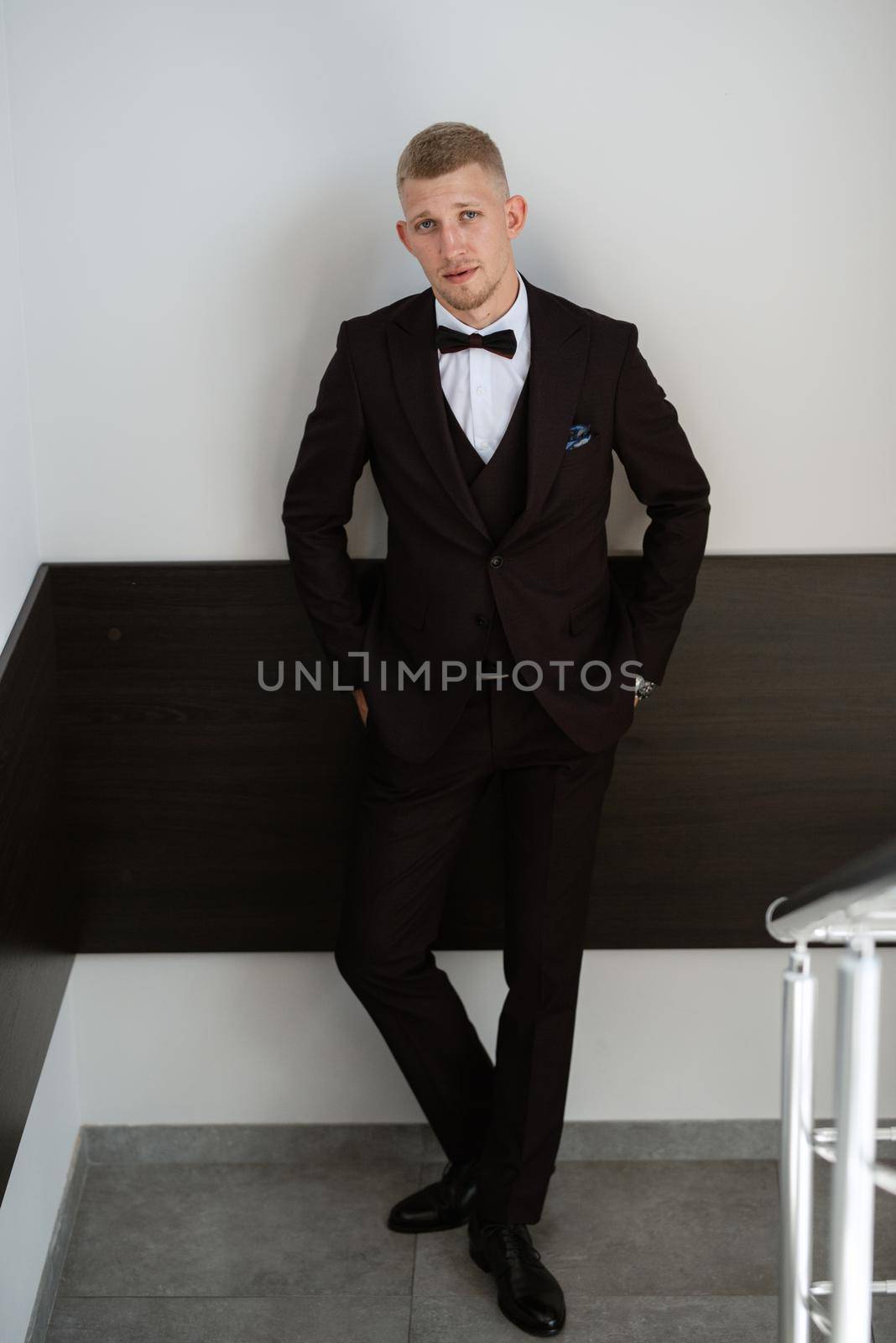 portrait of the groom in a brown three-piece suit with a bow tie on the wedding day