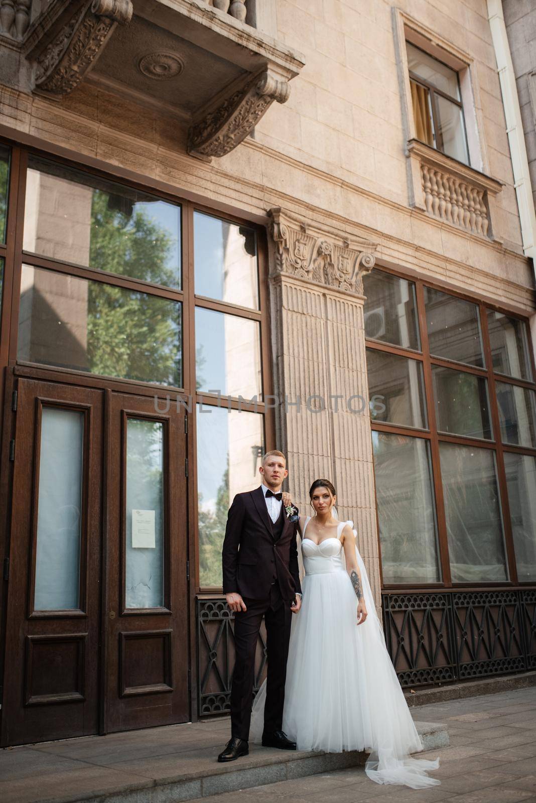 the groom in a brown suit and the bride in a white dress in an urban atmosphere