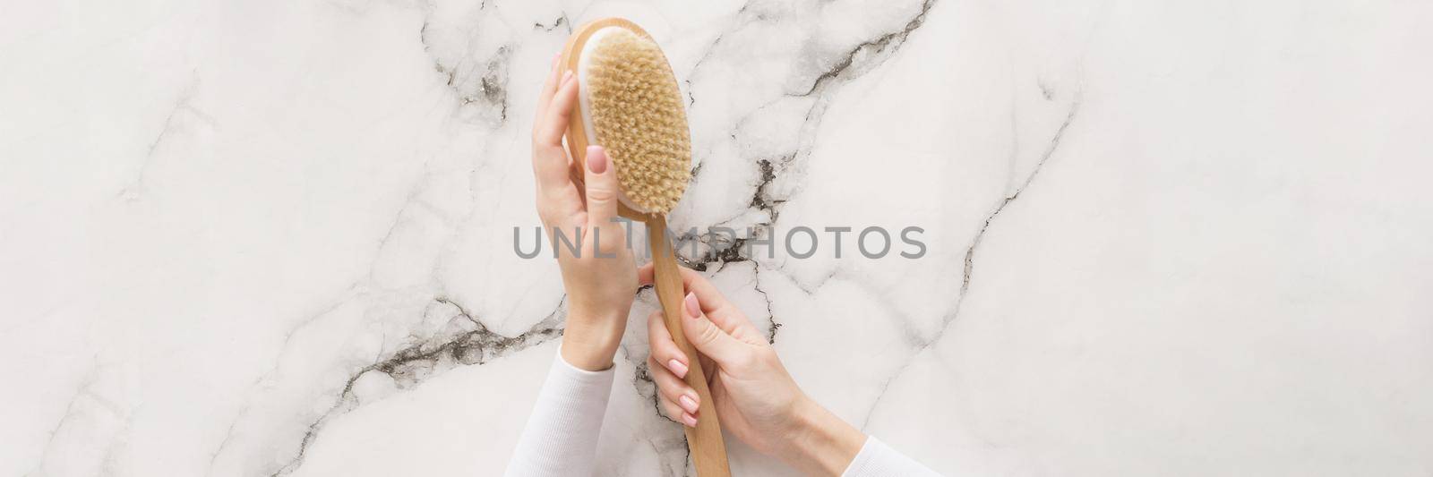 Brush for dry massage in the hands of a girl on a marble background. Brush for scrubbing the body, bringing it in order, against cellulite. Web banner.