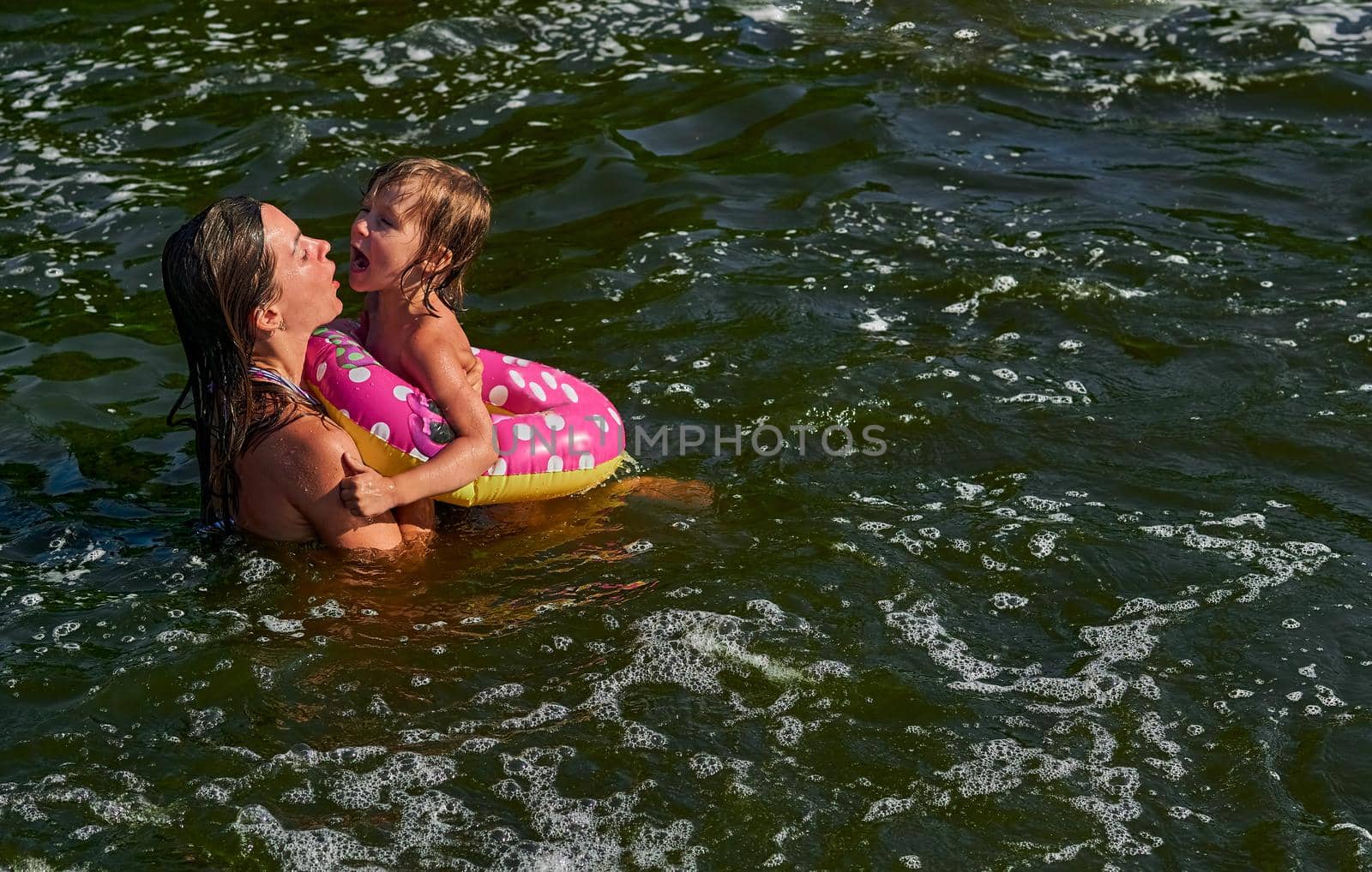 propel the body through water by using the limbs,by using fins, tail, or other bodily movement.Cute girl on a swimming circle bathes with her mother protecting her in the sea.
