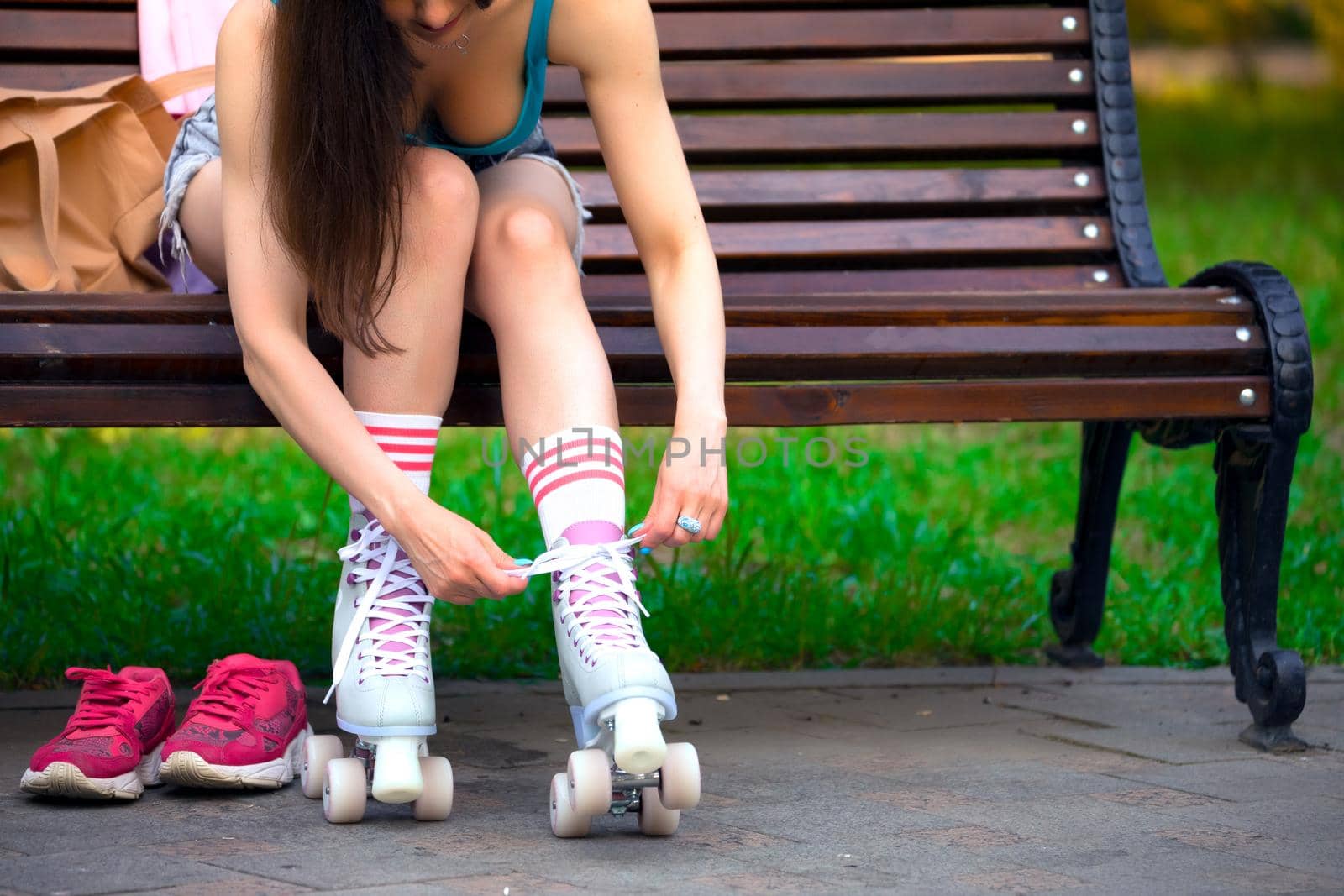 Female skater binds the roller skates on the bench in a park by Nobilior