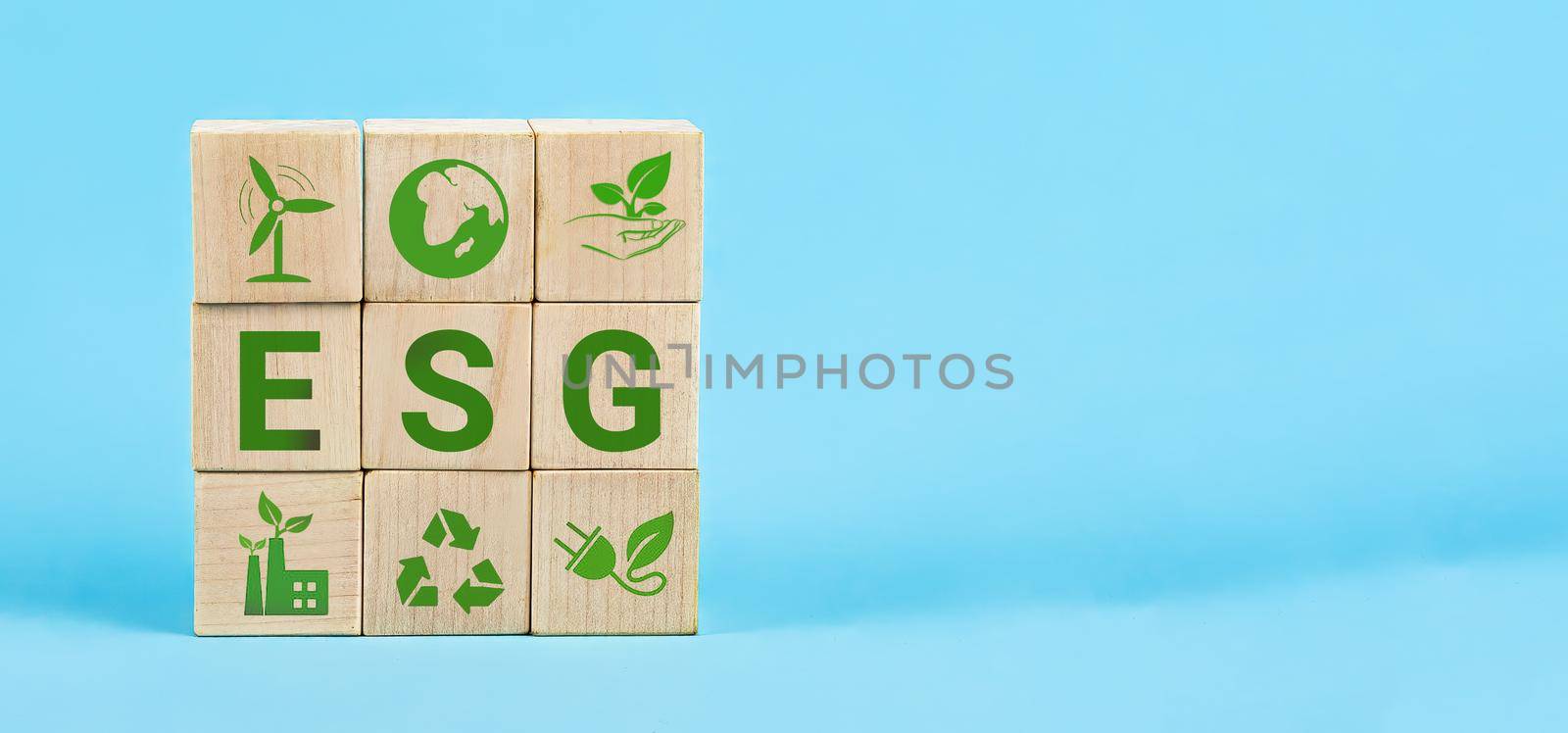 ESG Words on a wood cubes. ESG concept of environmental, social and governance. Wooden cube with abbreviation ESG standing with other icons on blue background.