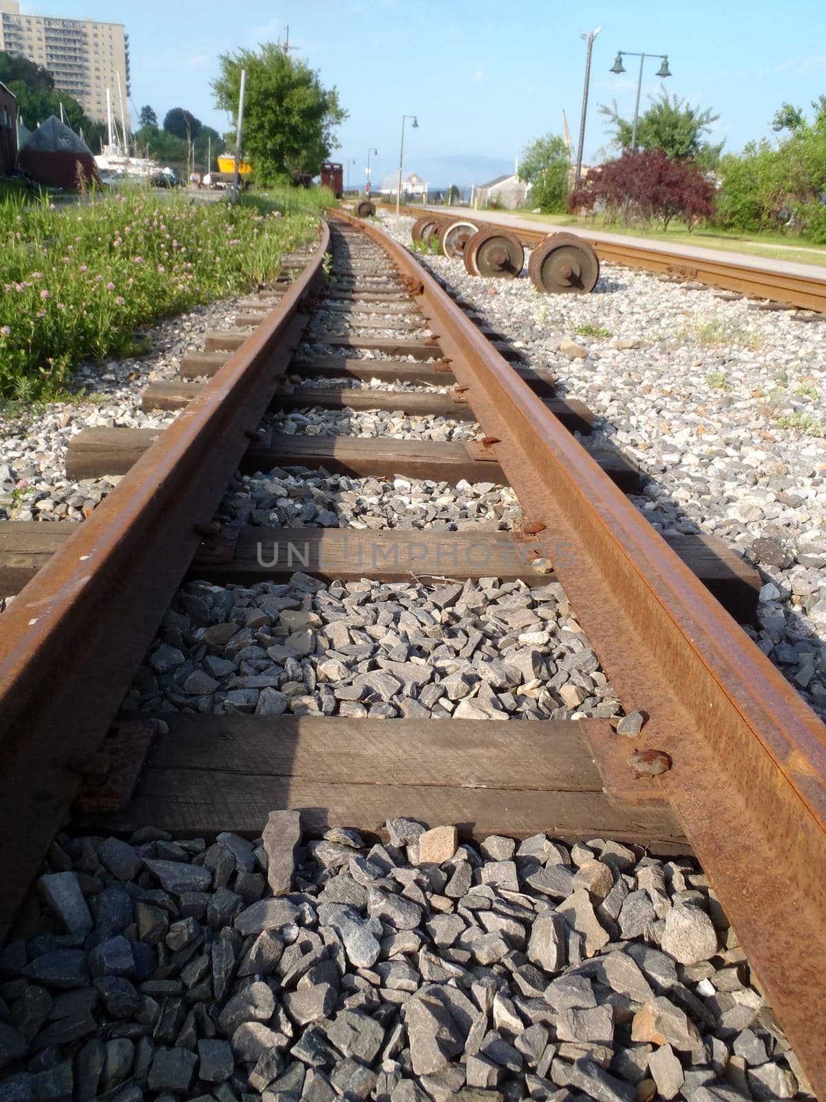 Railroad tracks running into distance with through Portland, Maine with grass growing and rocks in between tracks.