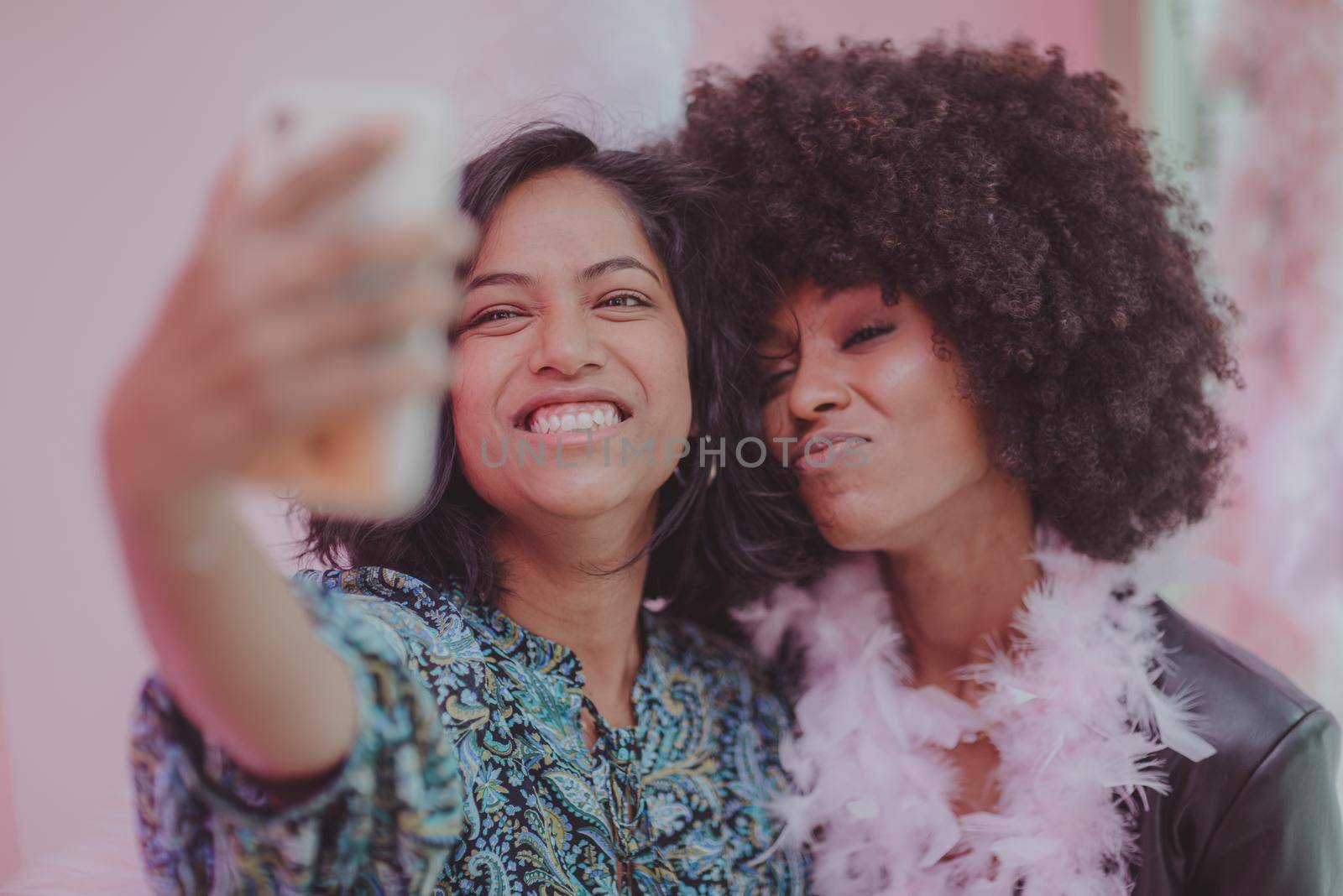 Couple of young south asian woman and african amercian woman having fun taking selfies in a bar.