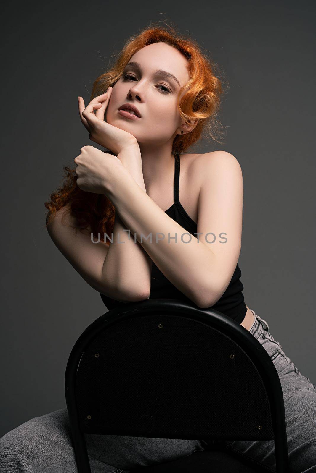 Cheerful redhead female model with ginger hair in casual outfits smiling and looking at camera while sitting on chair