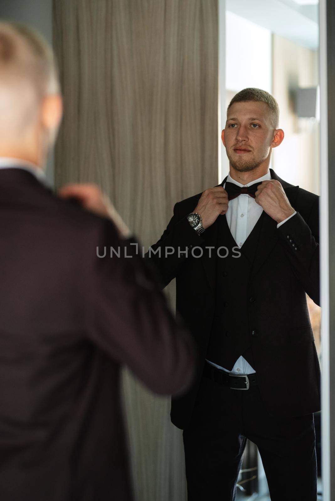 portrait of the groom in a brown three-piece suit with a bow tie on the wedding day