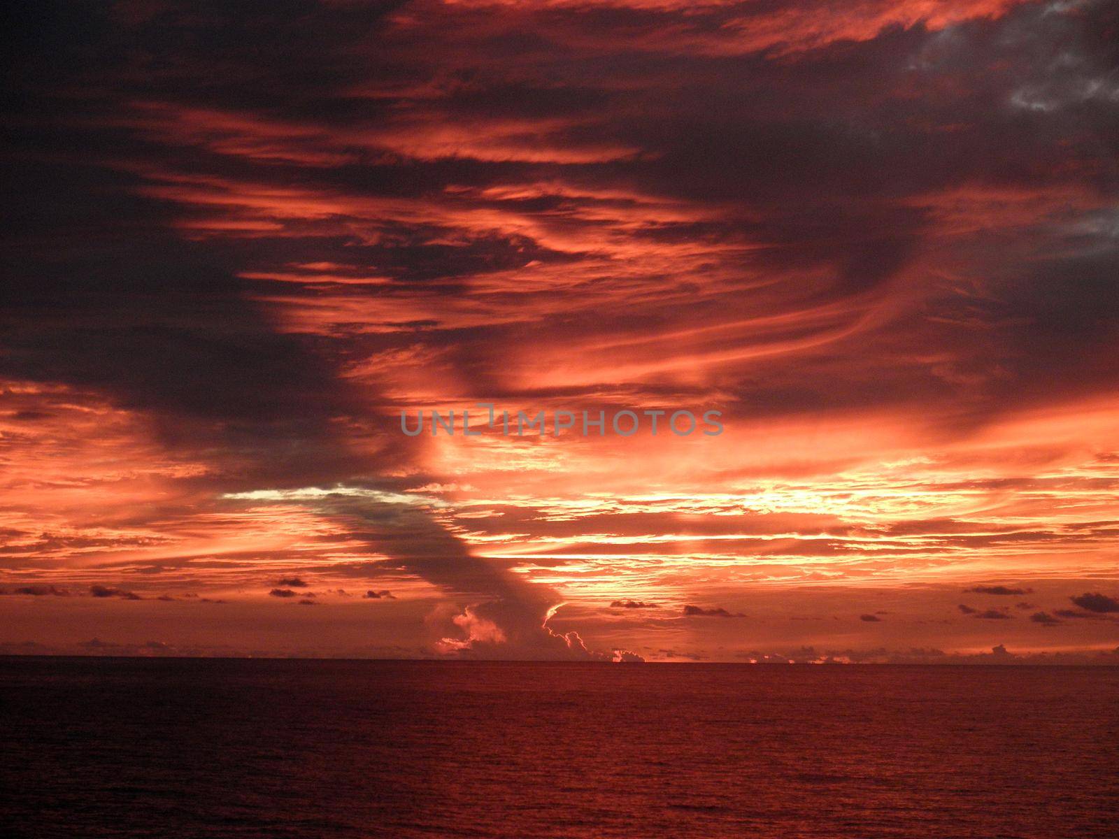 Dramatic Red light shines through the clouds as the sunsets over the pacific ocean by EricGBVD