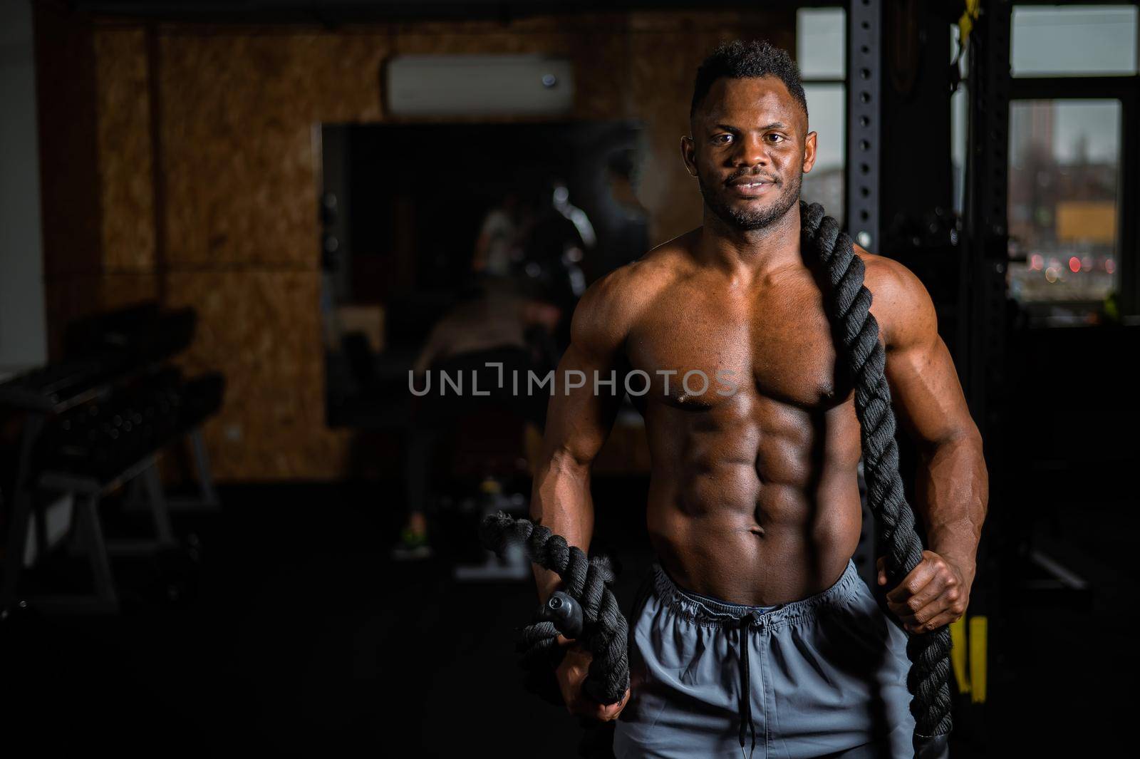 Muscular african american man posing with rope in gym