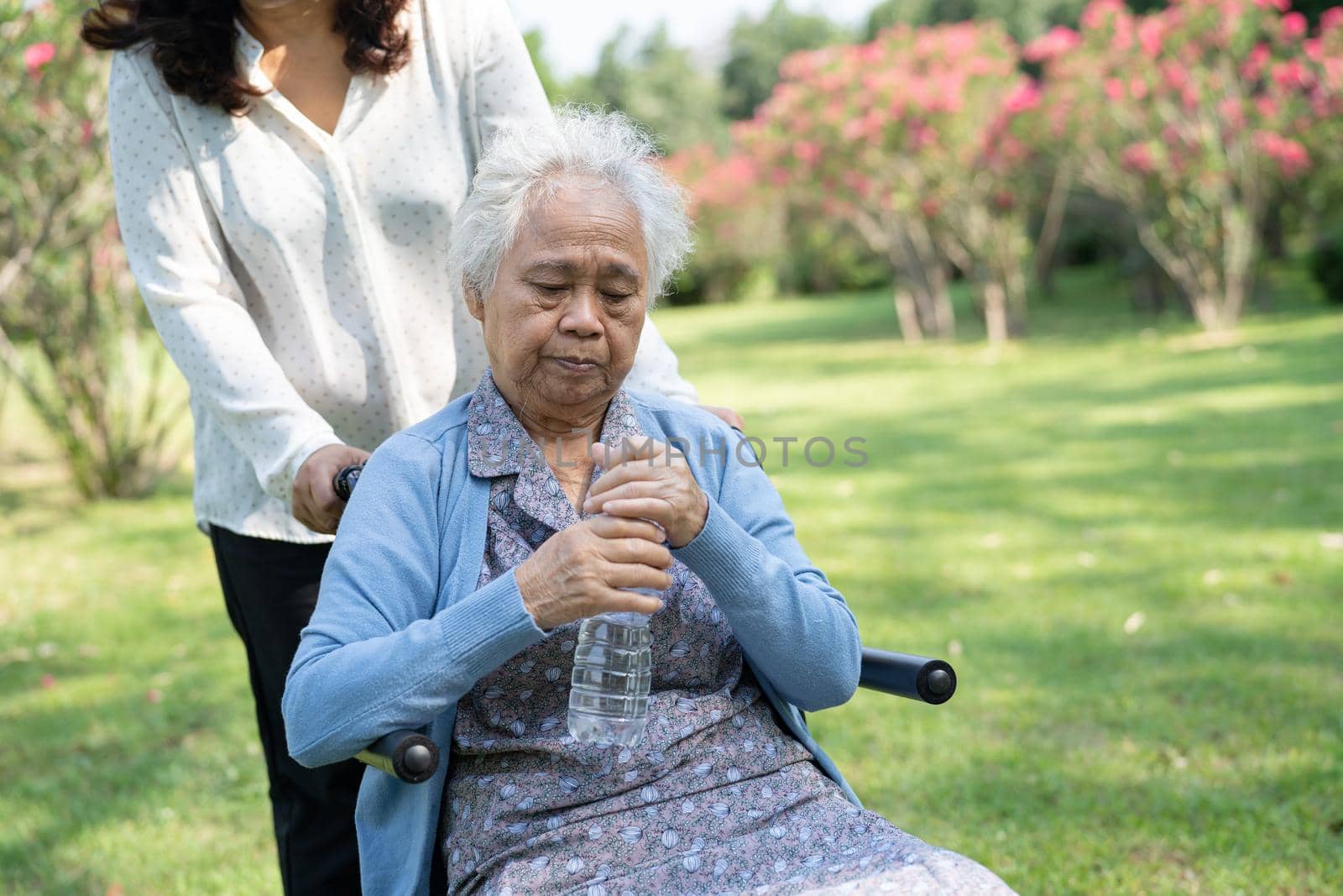 Caregiver help and care Asian senior or elderly old lady woman patient sitting on wheelchair and drink water in park.