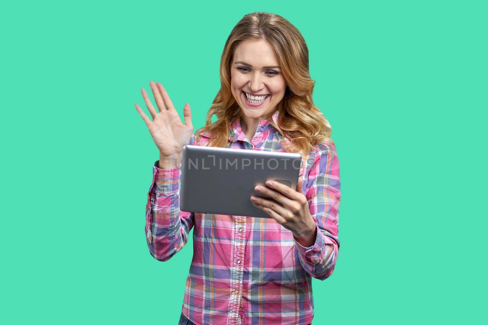 Young cheerful woman having a video call on color background. Young smiling woman holding digital tablet and waving with hand.