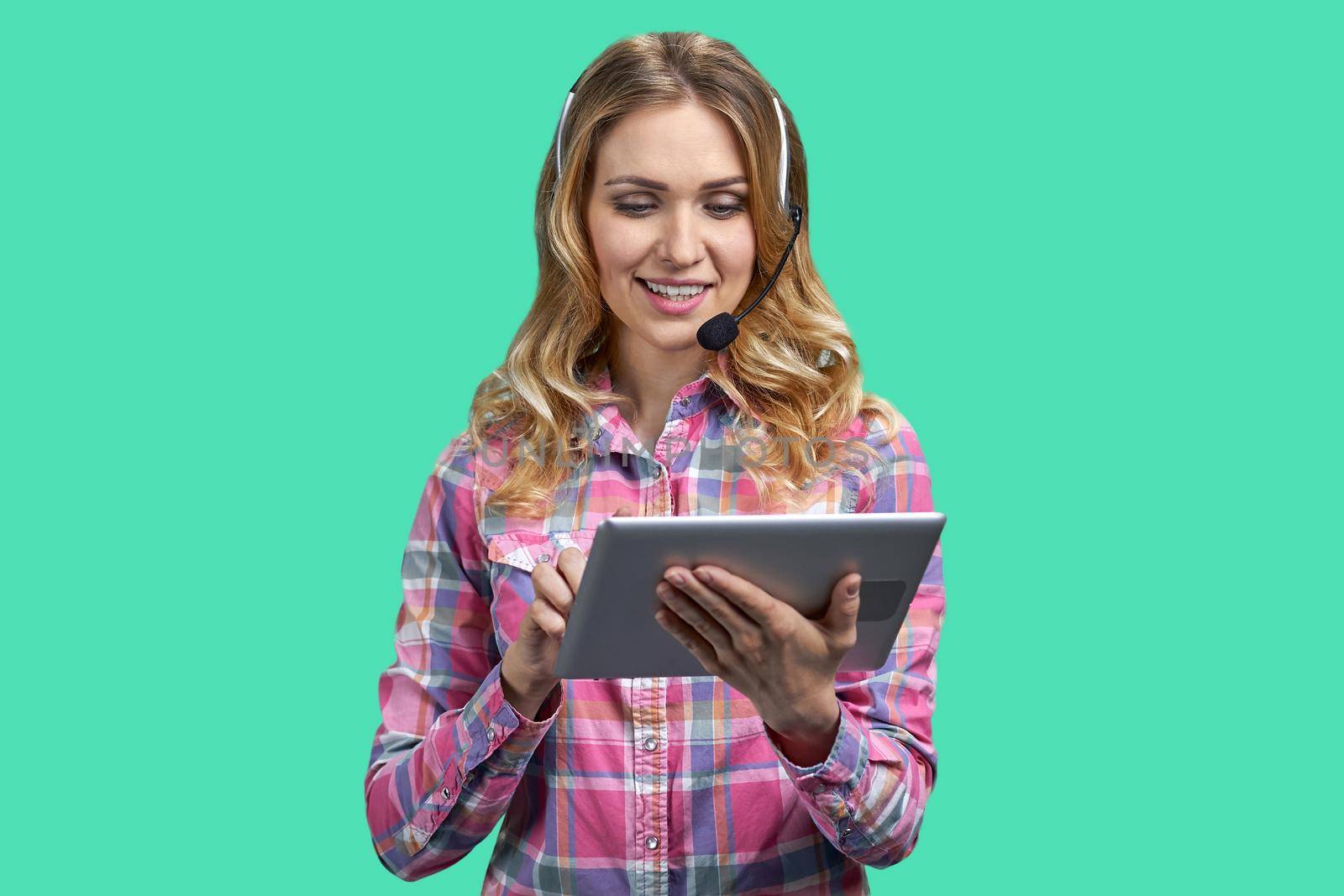 Customer service worker with headset using computer tablet. Female customer support agent working on tablet pc against green background.