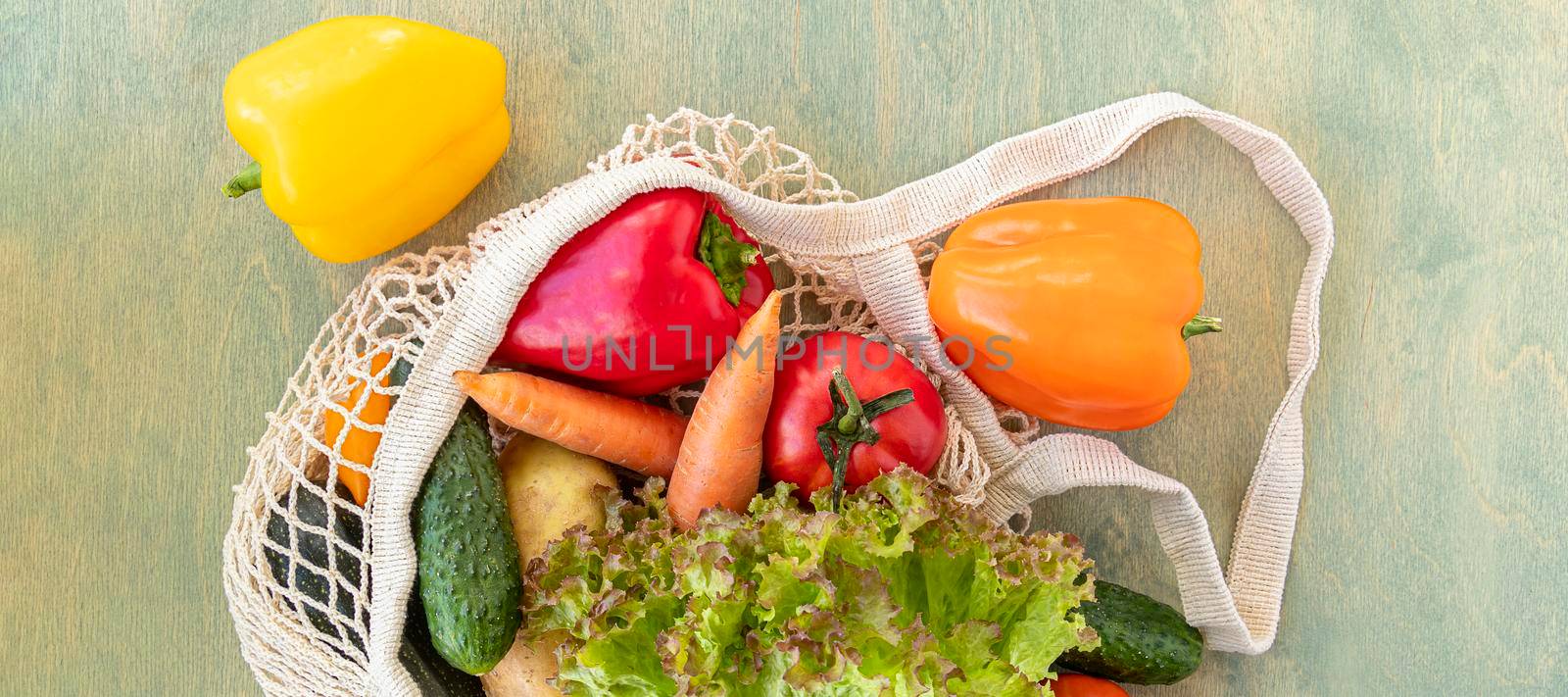 banner with Top view of mesh shopping bag with organic eco vegetables on green wood background. Caring for the environment and the rejection of plastic concept. flat lay