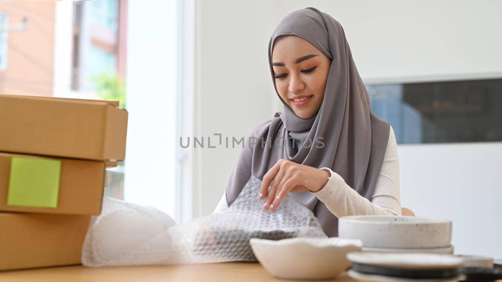 Young asian muslim woman in headscarf preparing packages for delivery to customers. E-commerce, Online selling concept.