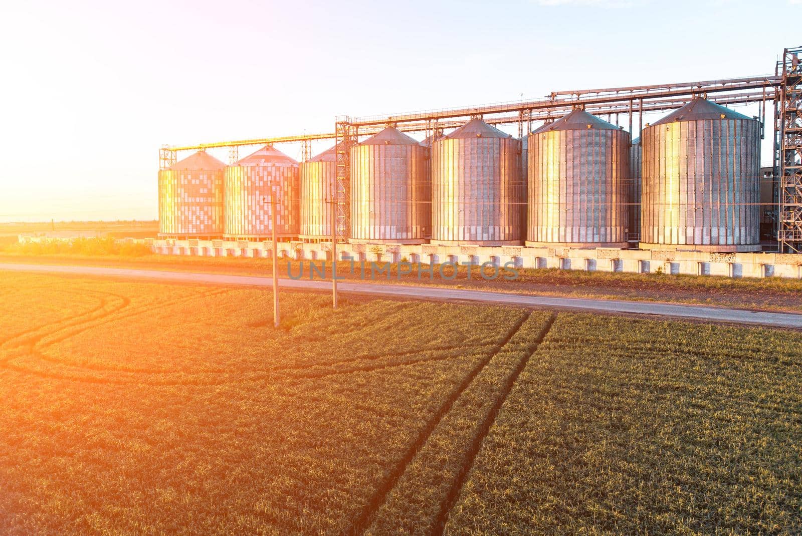 Grain elevator. Metal grain elevator in agricultural zone. Agriculture storage for harvest. Grain silos on green nature background. Exterior of agricultural factory