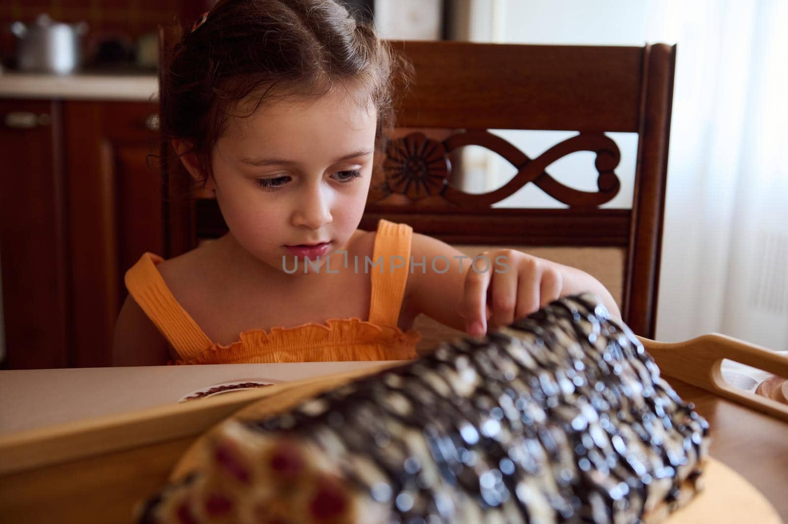 Cheerful and funny European little girl sitting a dining table with served homemade cake, cherry pie, sweet dessert- Monastery hut in the home kitchen interior