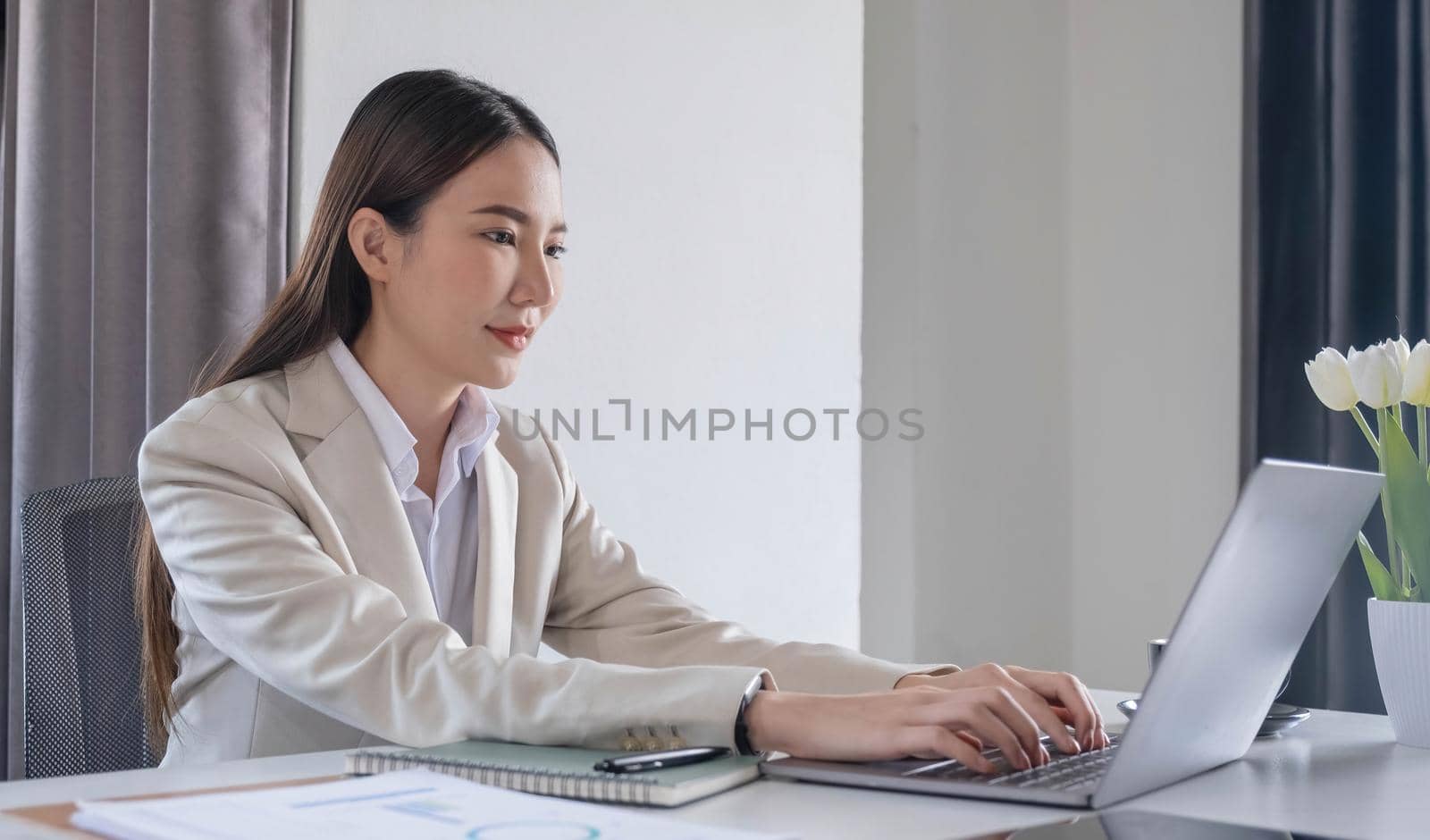 Front view of a beautiful Asian businesswoman working on a tablet coffee cup placed on the office table. by wichayada