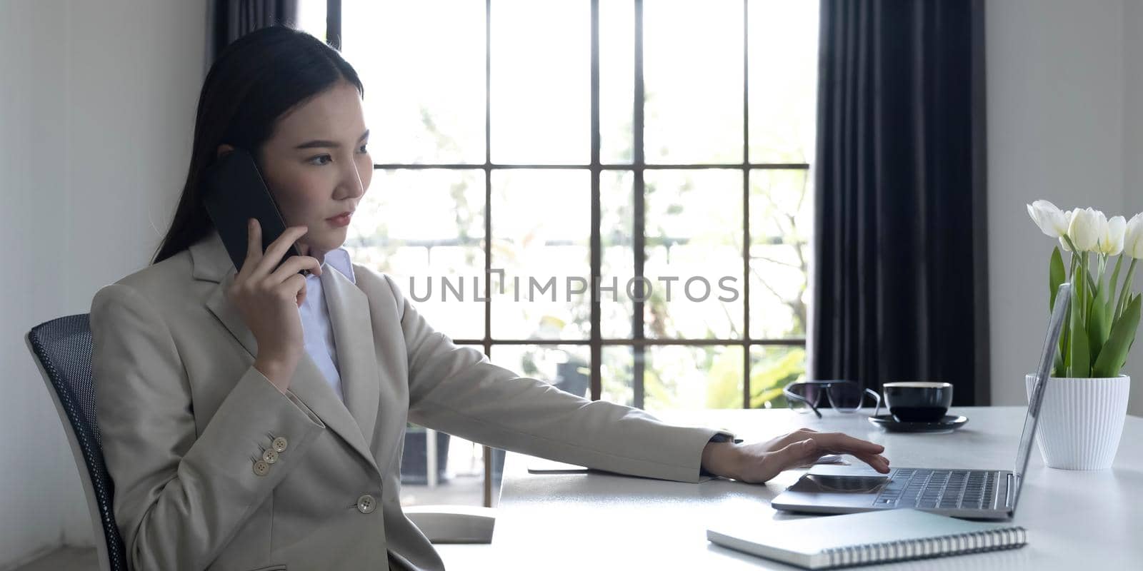 Asian businesswoman talking on a cell phone with a serious expression while working in the office by wichayada
