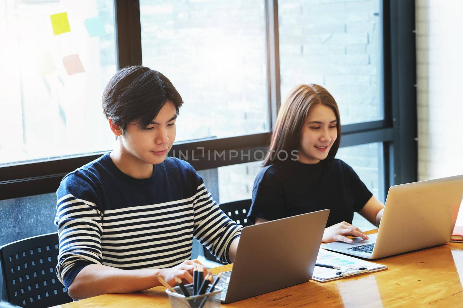 Male and female employees working with laptop computer in the office. by Manastrong