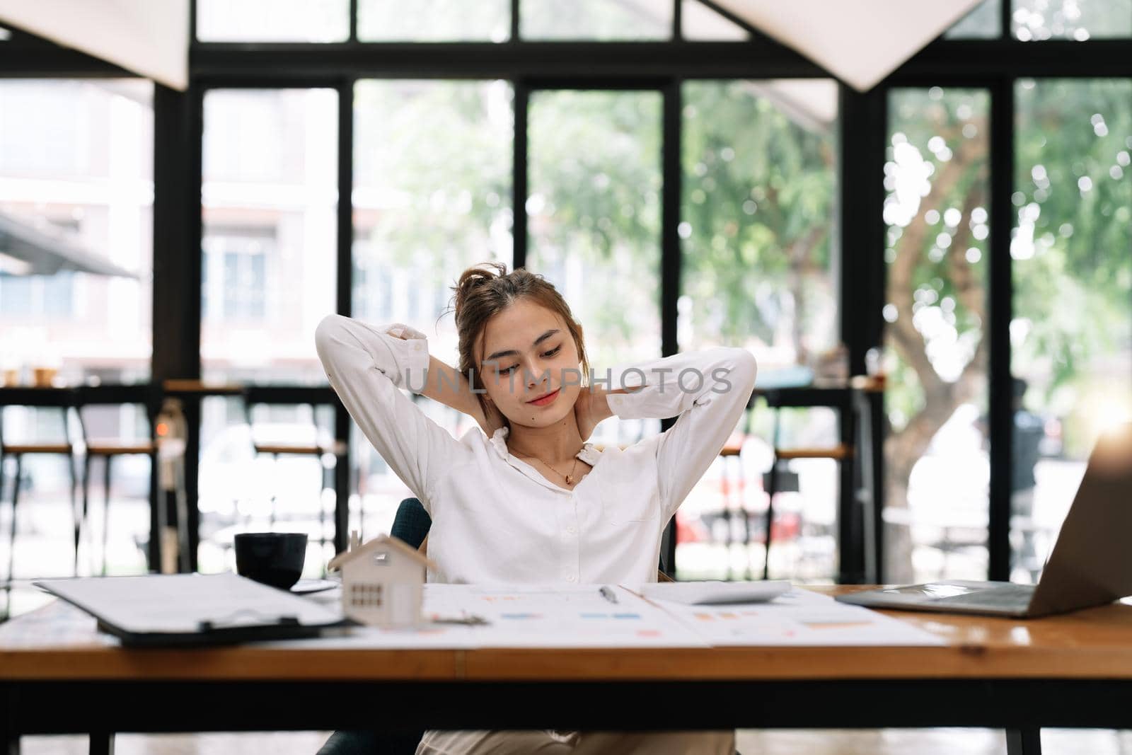 Happy young asian businesswoman relaxing with hands behind head at office desk. Daydreaming concept.