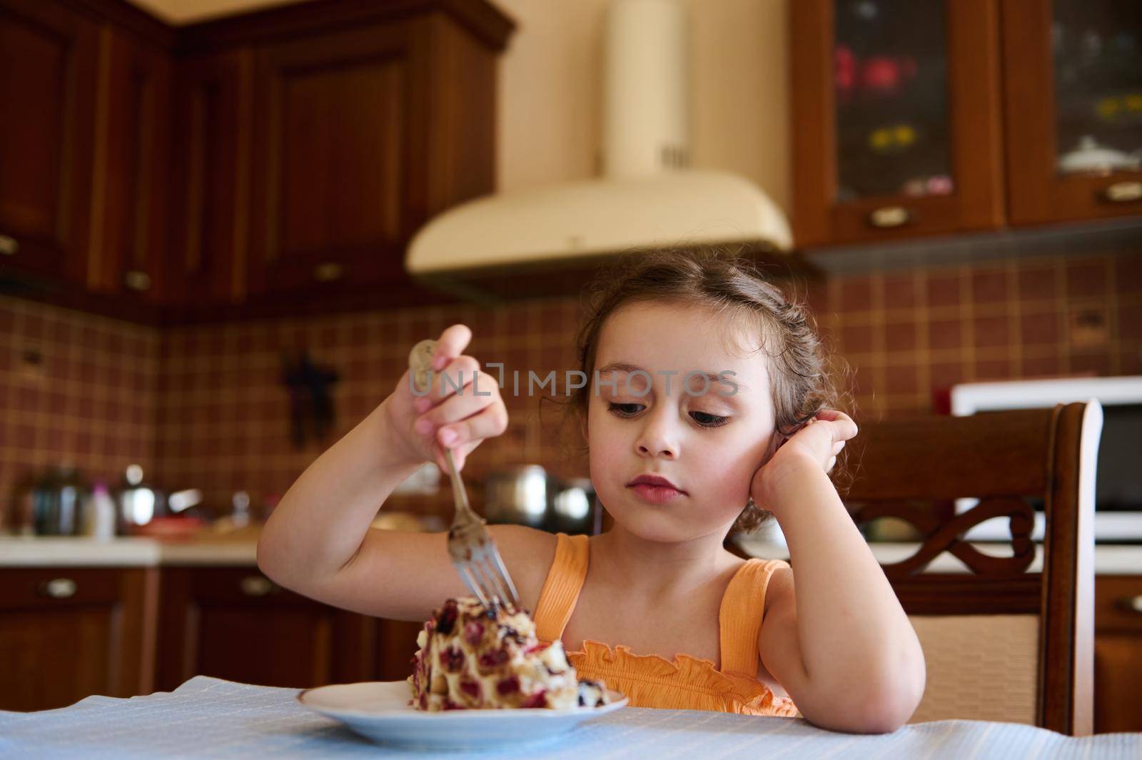 Adorable European 5 years old girl eating delicious sweet dessert, a cherry cake - Monastic log, in the home wooden kitchen