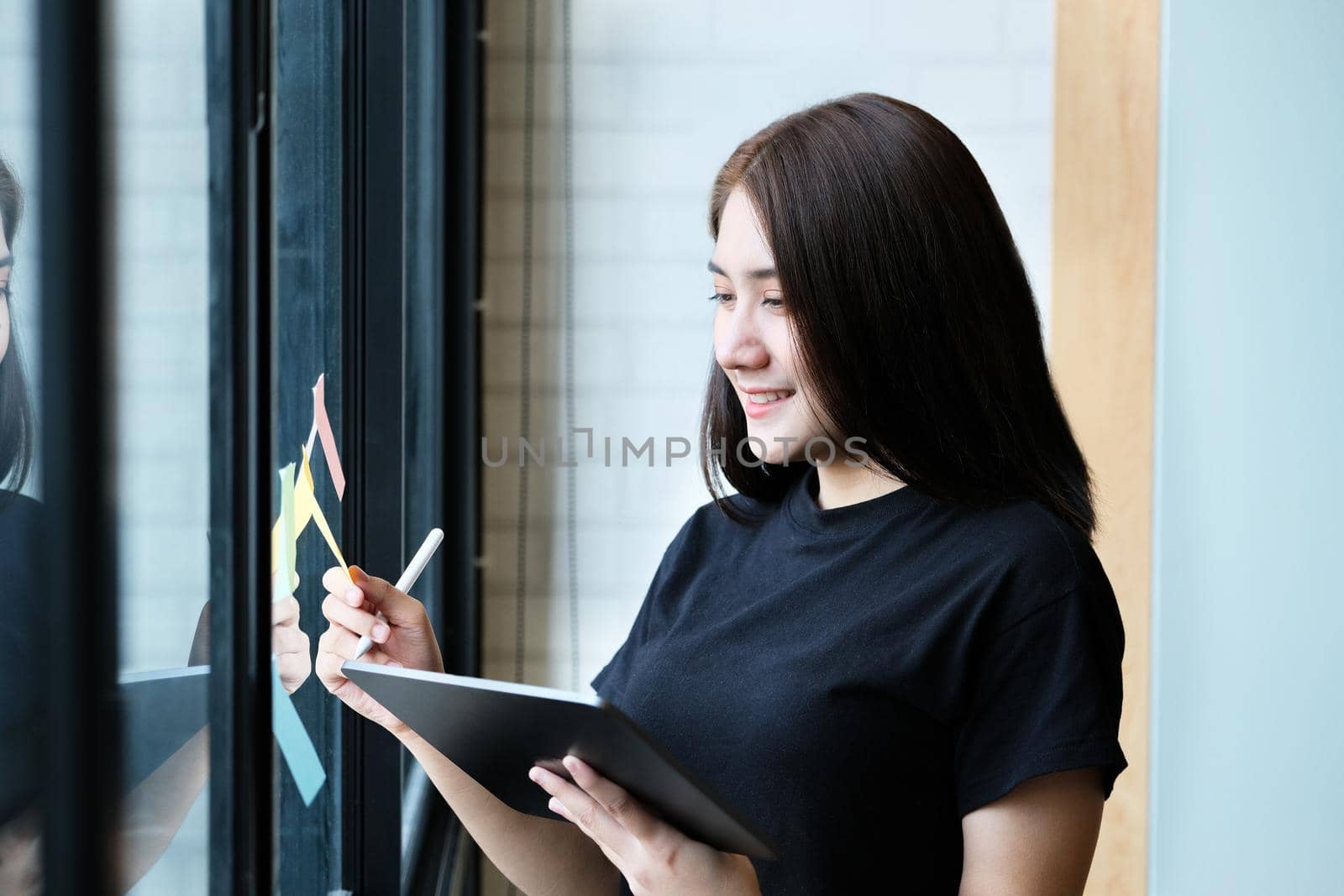 A female company employee uses a tablet and notepad to analyze company budgets. by Manastrong