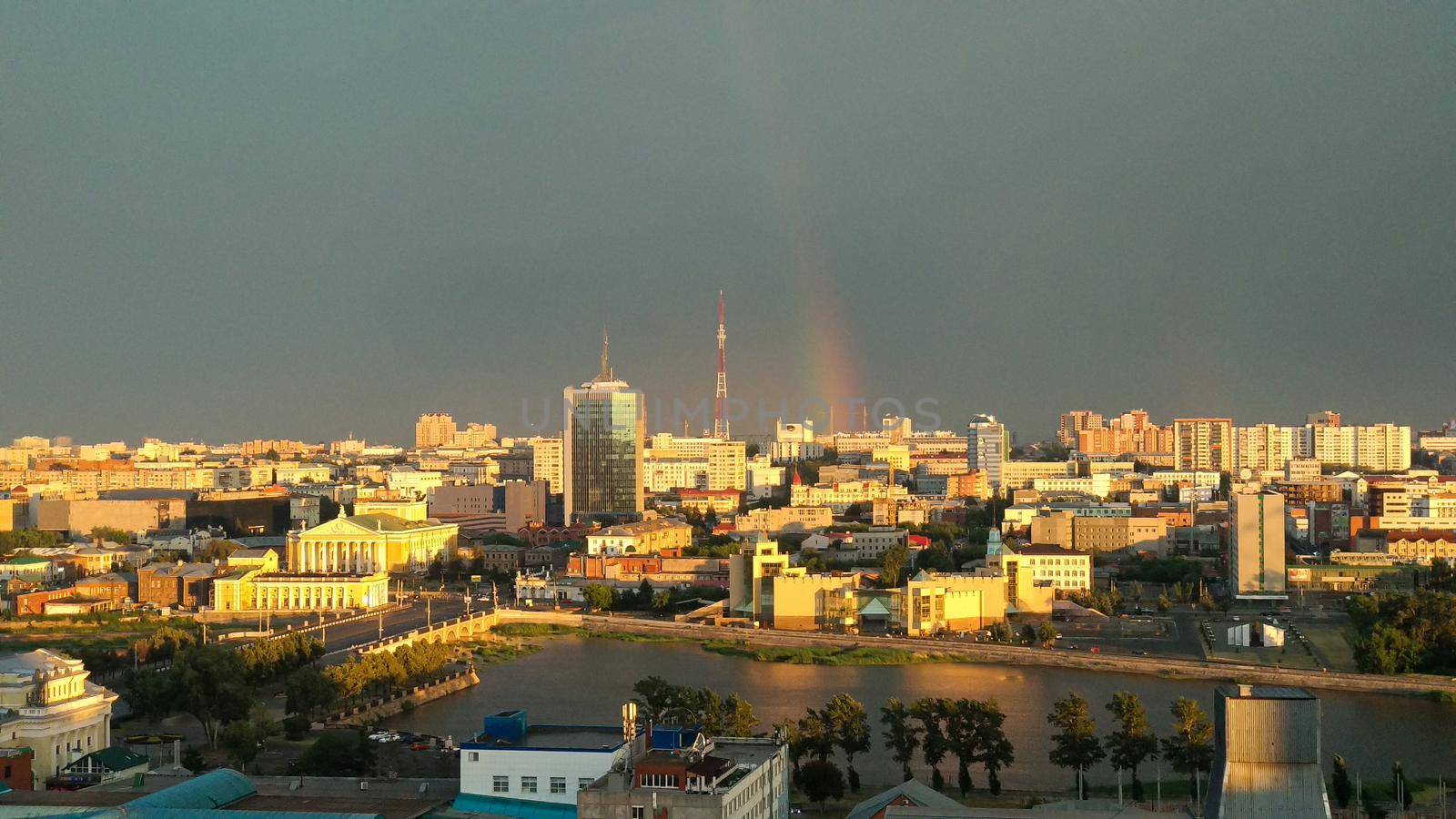 Cityscape illuminated by evening sunlight and a rainbow on a cloudy sky by ProjectStockman