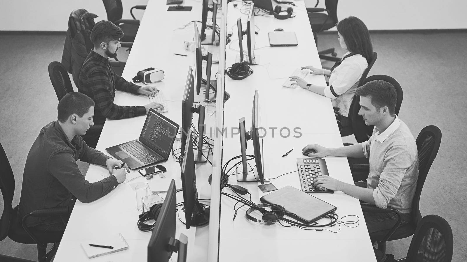 Young professionals working in modern office. Group of developers or programmers sitting at desks focused on desktops and laptops in IT company open space. Team at work. High quality image.