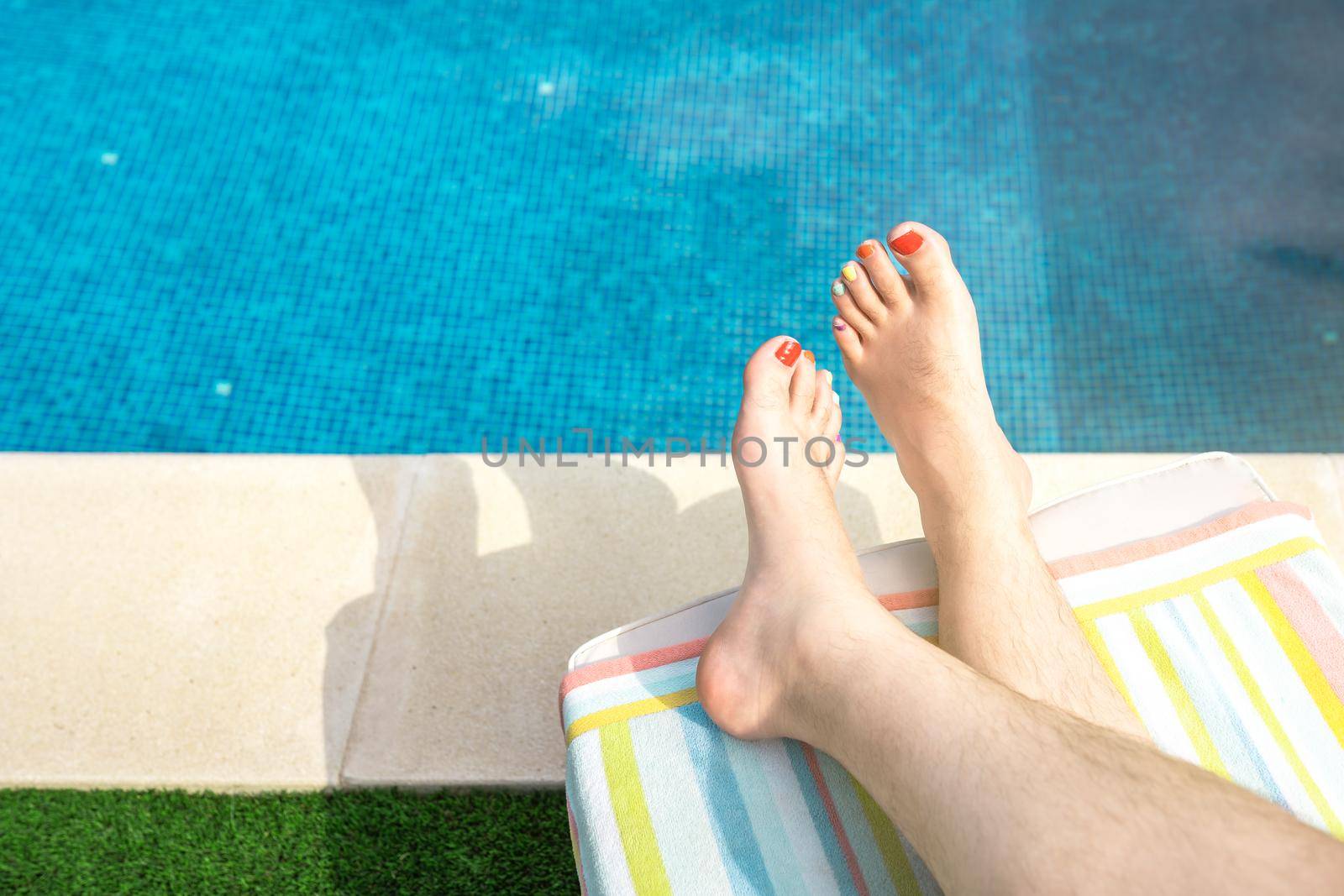 Close-up of the bare feet of a young man lying on a deckchair in a swimming pool. barefoot man with his nails painted in LGTBIQ colours. concept of travel and leisure. natural sunlight, outside, garden with swimming pool.