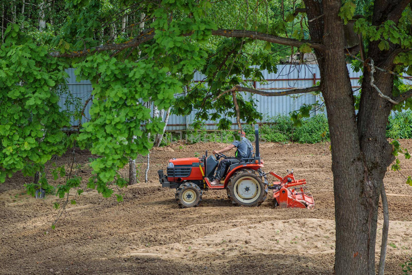A farmer on a mini tractor loosens the soil for the lawn. Land cultivation, surface leveling.