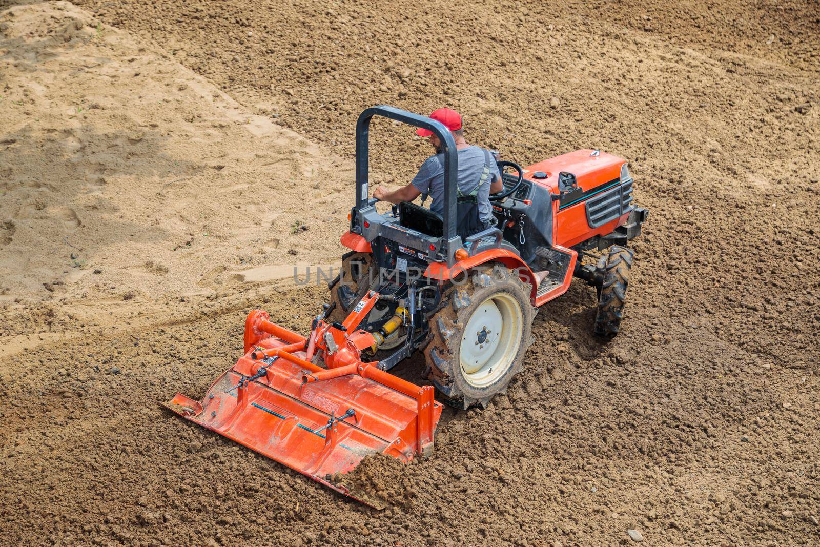 A farmer on a mini tractor loosens the soil for the lawn. Land cultivation, surface leveling.