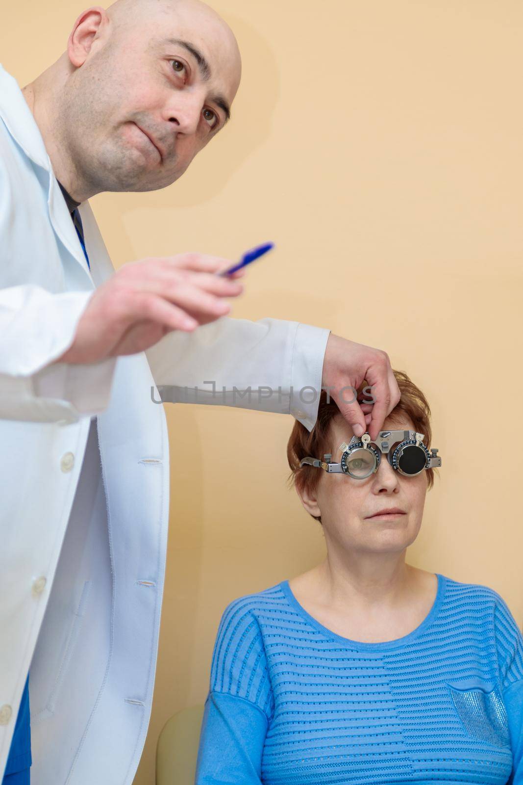 A male optometrist checks the eyesight of an adult woman with a trial frame by Yurich32