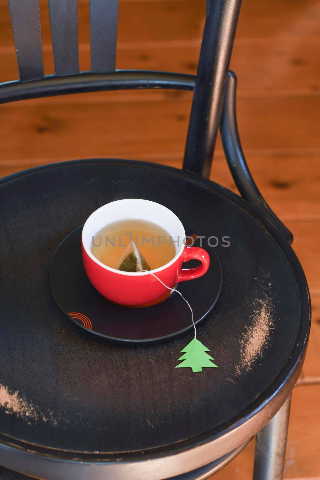 A red cup with tea is wrapped in a warm Christmas sweater, a tea bag label in the form of a green Christmas tree. High quality photo