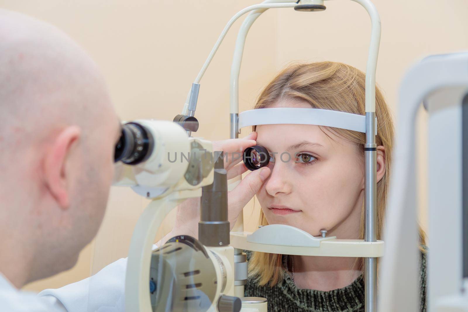 A male ophthalmologist checks the eyesight of a young girl using a modern device with a light beam by Yurich32