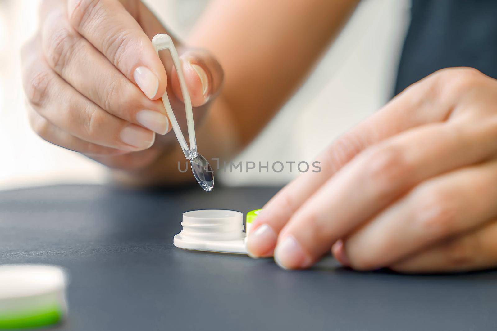 Woman holds the contact lens with tweezers.. Black background, close-up, lower angle