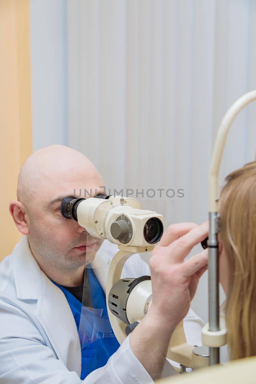 A male ophthalmologist checks the eyesight of a young girl using a modern device with a light beam.