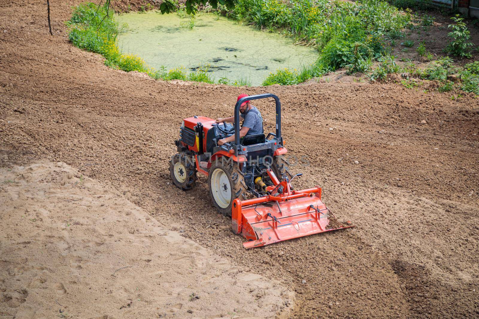 A farmer on a mini tractor loosens the soil for the lawn. Land cultivation, surface leveling.
