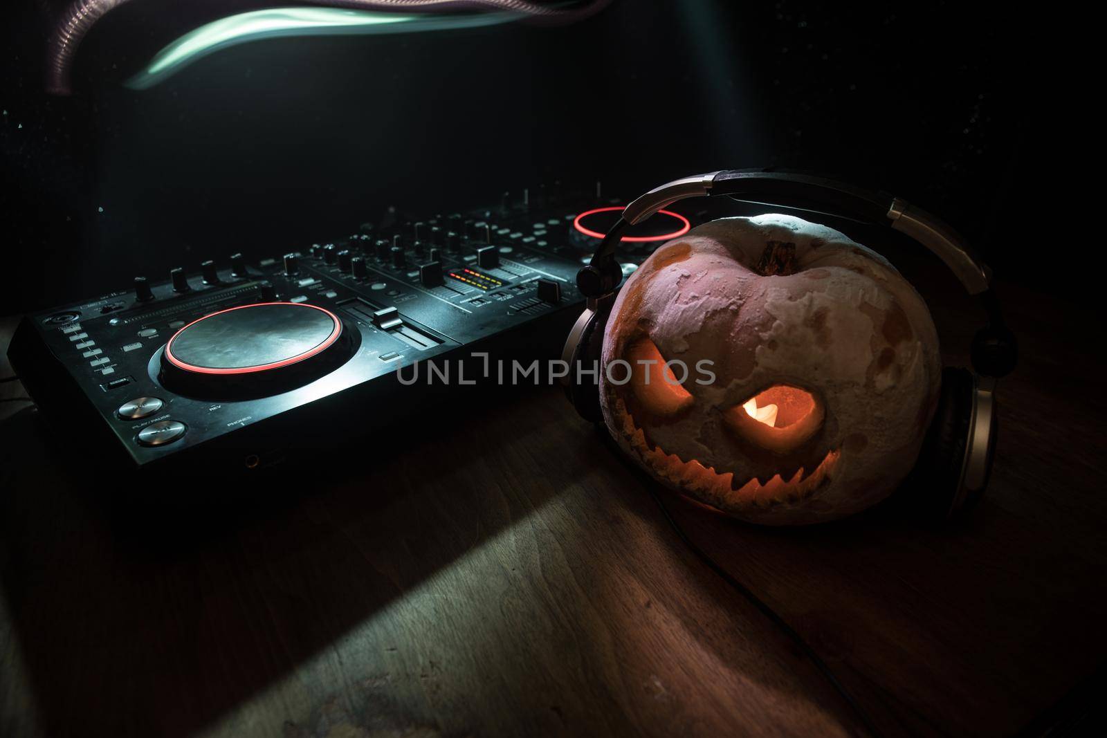 Halloween pumpkin on a dj table with headphones on dark background with copy space. Happy Halloween festival decorations by Zeferli