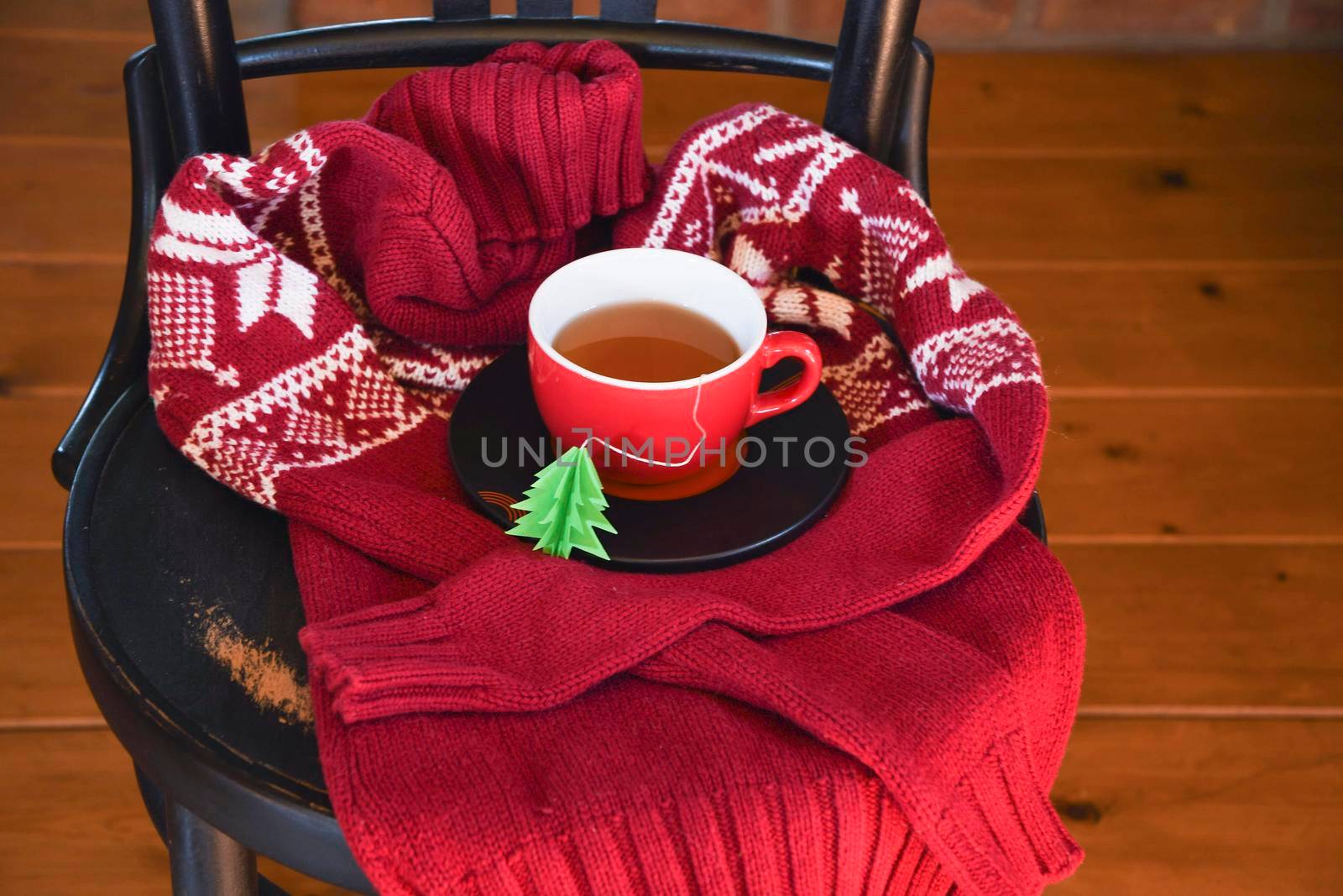 A red cup with tea is wrapped in a warm Christmas sweater, a tea bag label in the form of a green Christmas tree. High quality photo