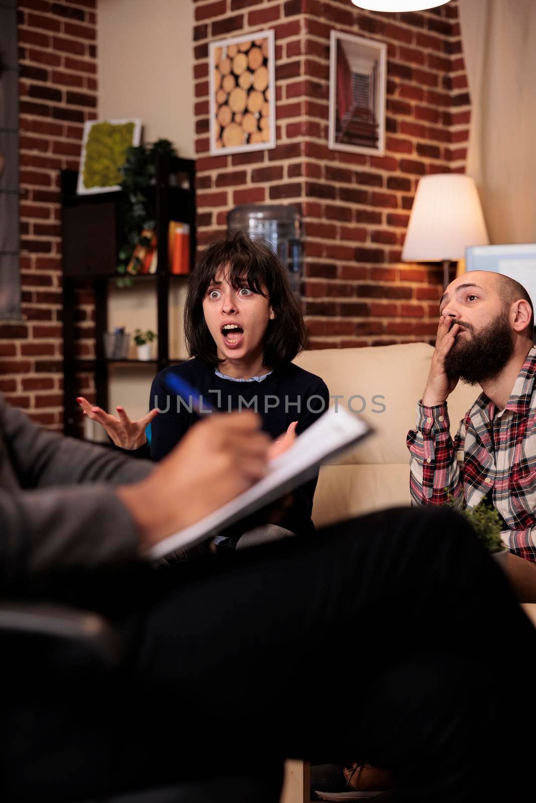 Male psychologist taking notes on paper at couple therapy with angry partners, talking about relationship issues. Doing psychoanalysis with married people, giving counseling advice.